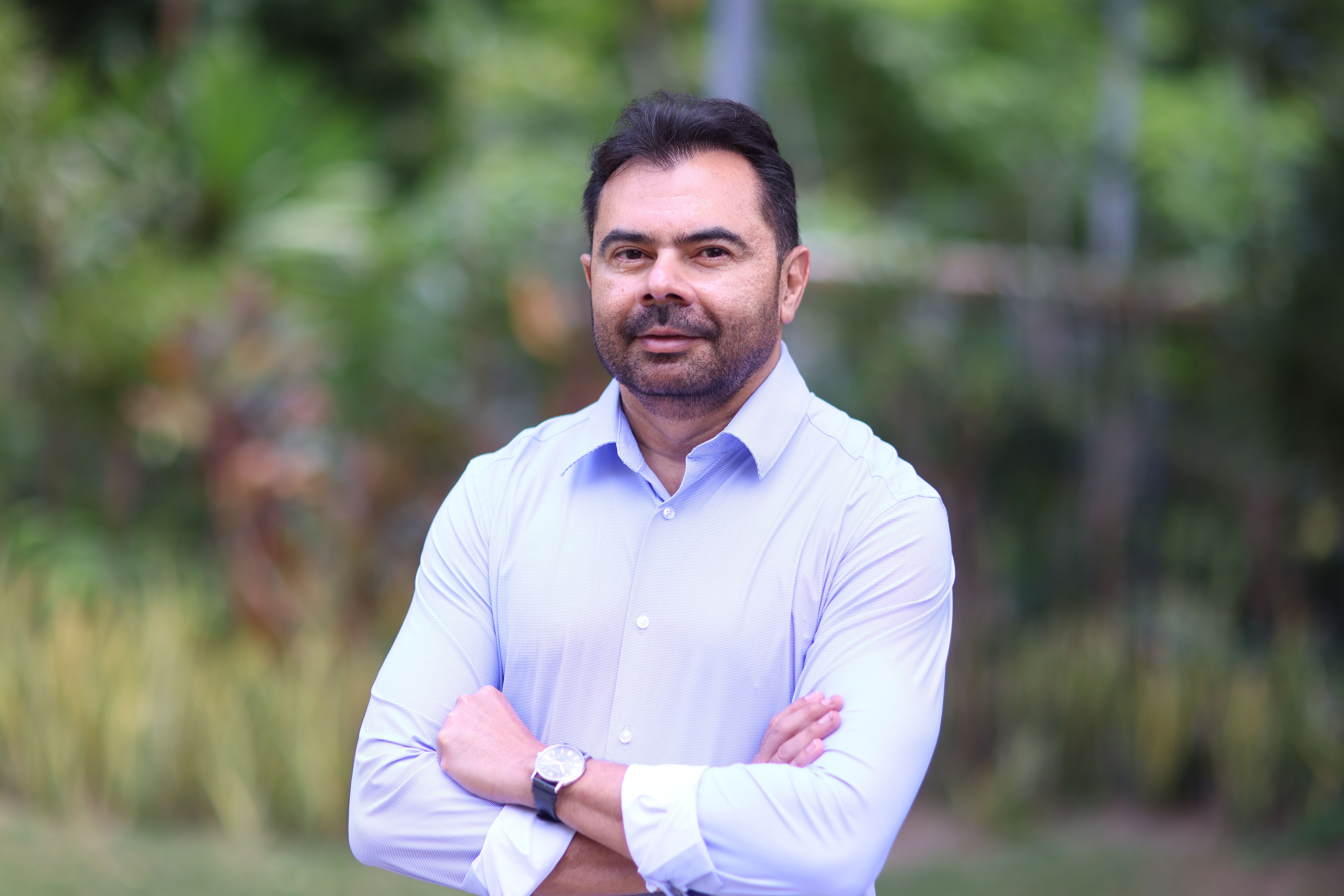 Idilvan Alencar posa para a foto, ele está de camisa azul clara e tem barba